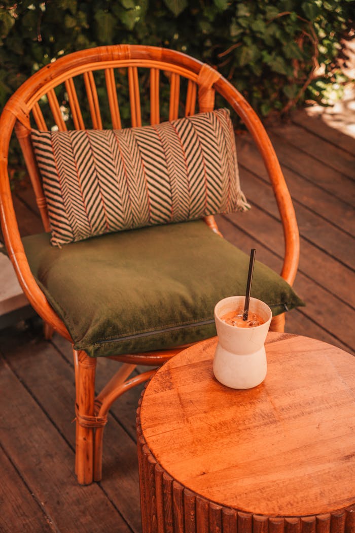Bamboo chair with cushion and refreshing drink on a wooden patio, relaxing outdoor setting.